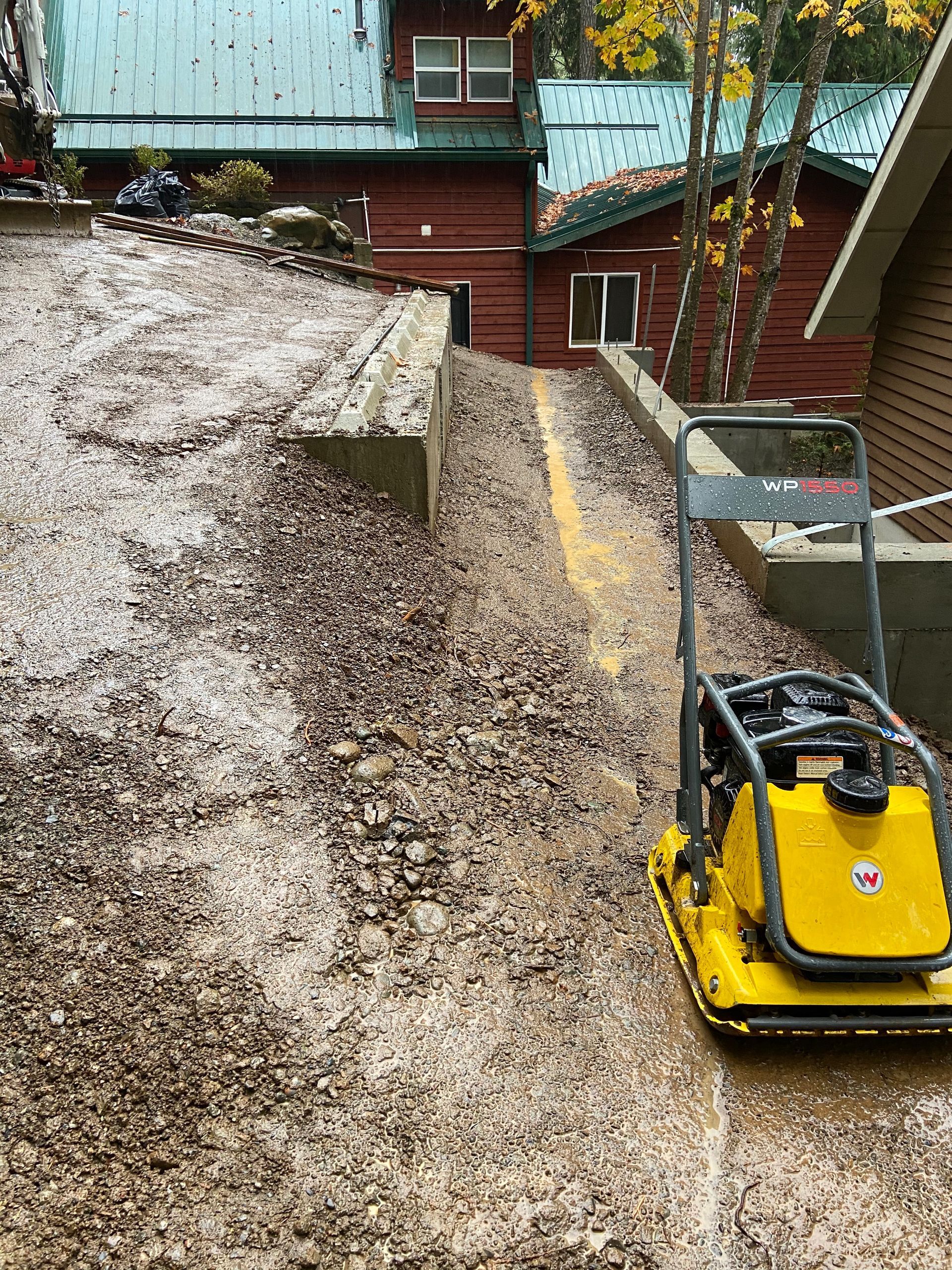 A yellow machine is sitting on top of a pile of gravel in front of a house.