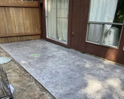 A patio with a sliding glass door and a wooden fence.