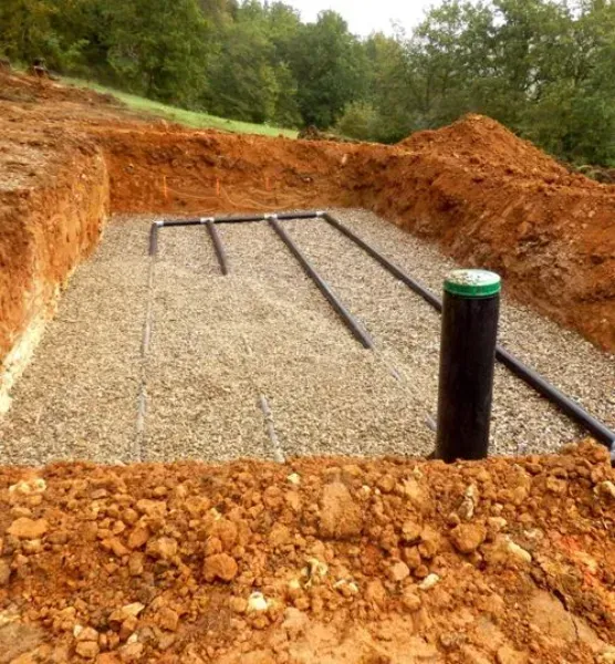 Gravel foundation pad in a dug-out site, with black drainage pipes and orange dirt walls.