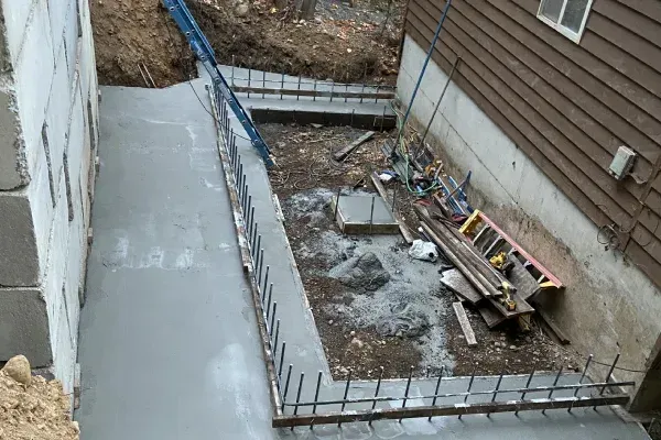 Concrete walkway and retaining walls under construction next to a house. Rebar visible.