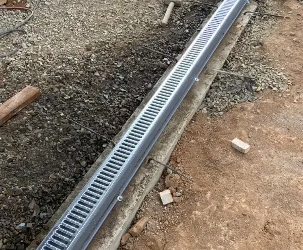 A metal drain is sitting on the ground next to a concrete curb.