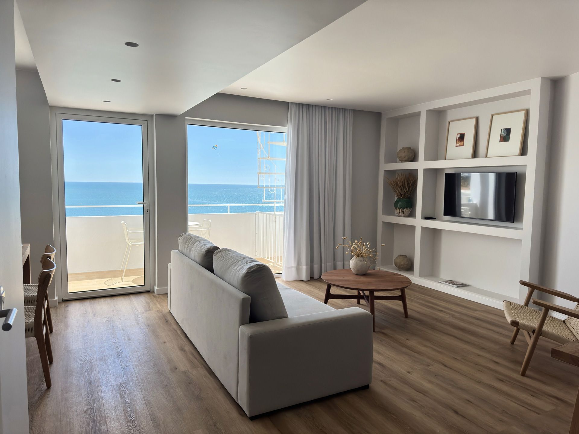 Uma sala de estar com sofá, mesa, televisão e varanda com vista para o oceano.