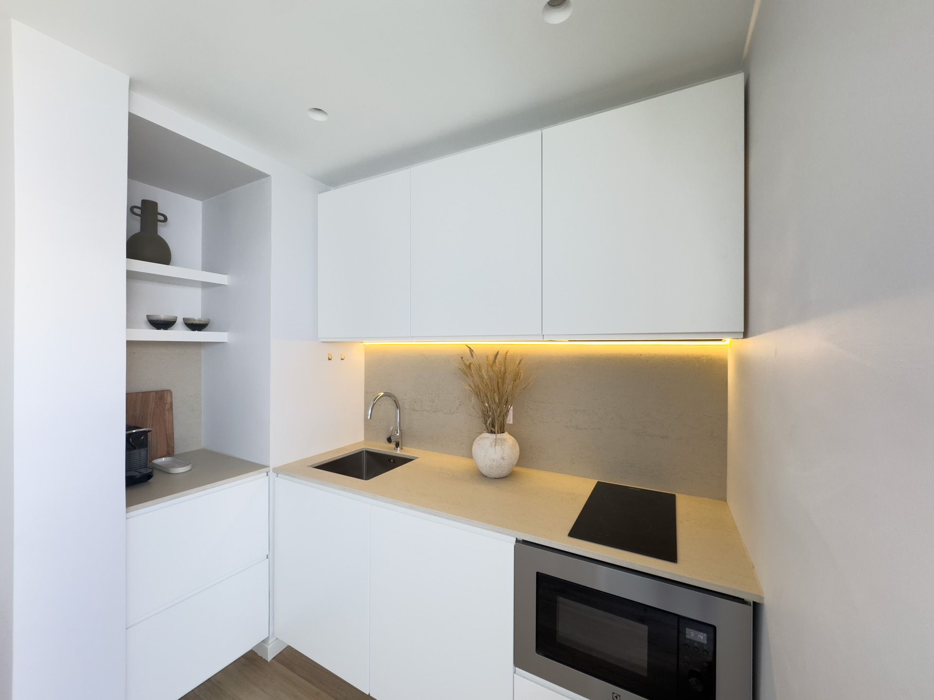 Uma pequena cozinha com armários brancos, uma pia e um micro-ondas.