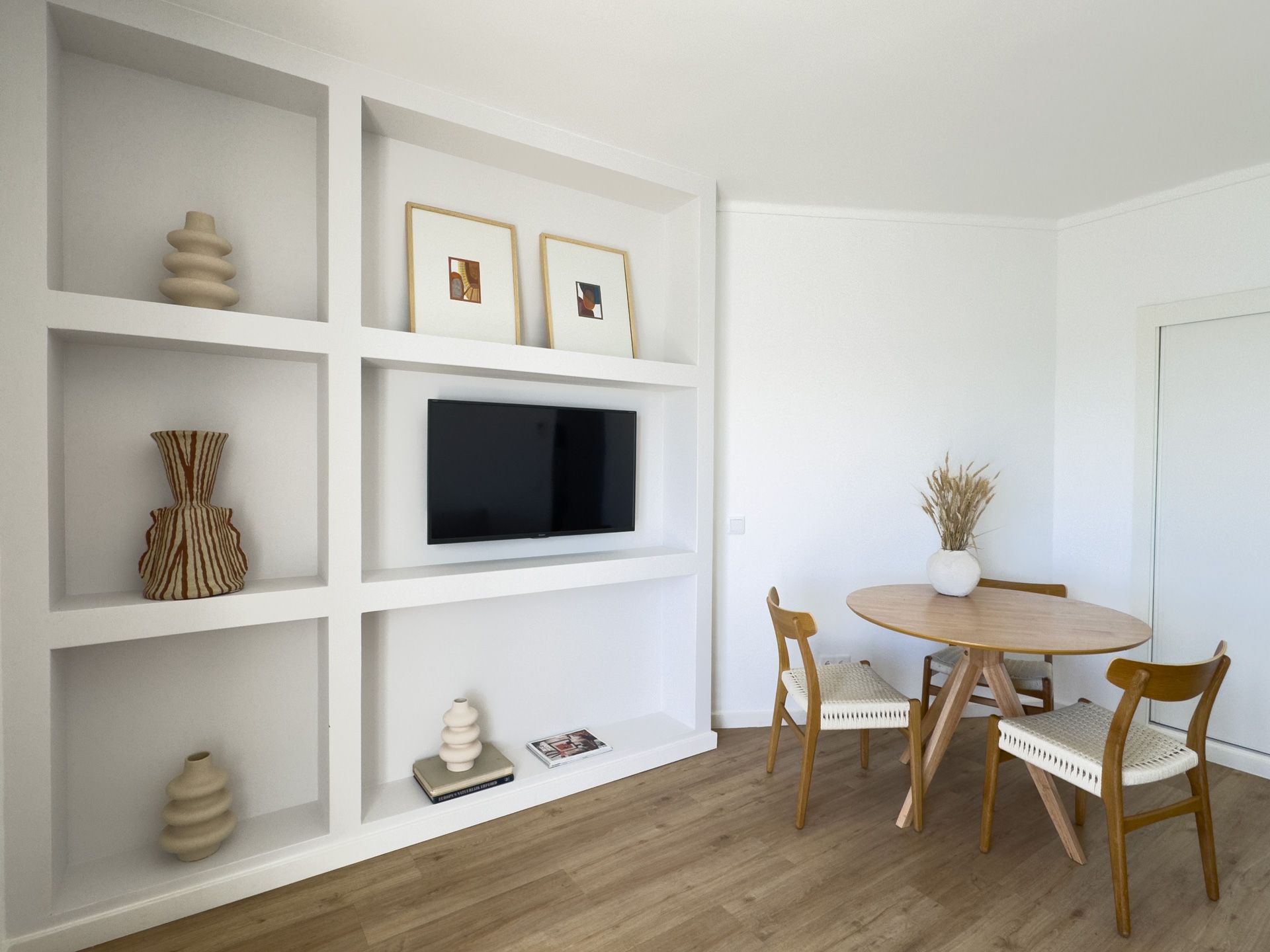 Uma sala de estar com mesa e cadeiras e uma TV de tela plana na parede.