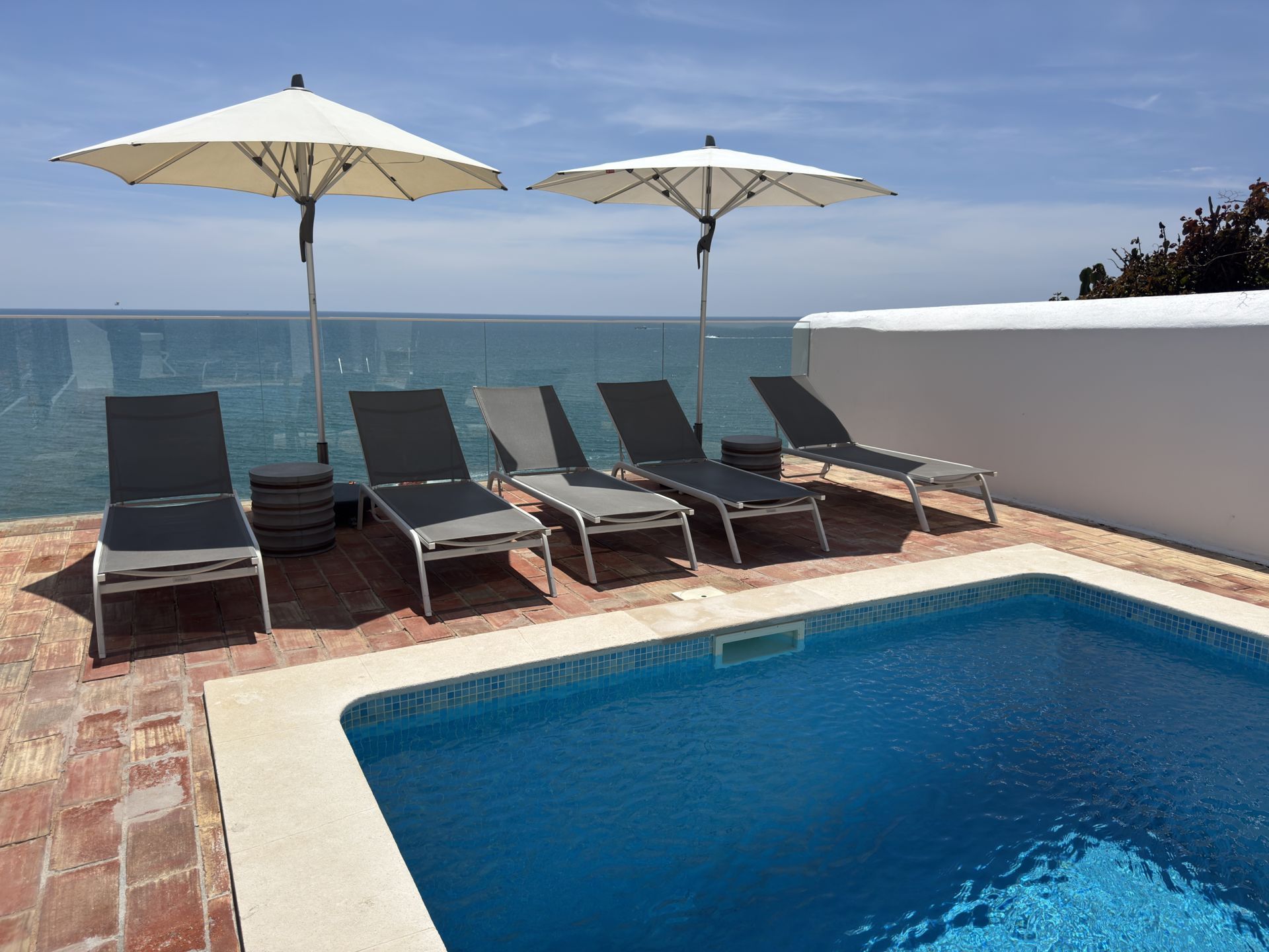 Uma piscina cercada por cadeiras e guarda-sóis com vista para o oceano