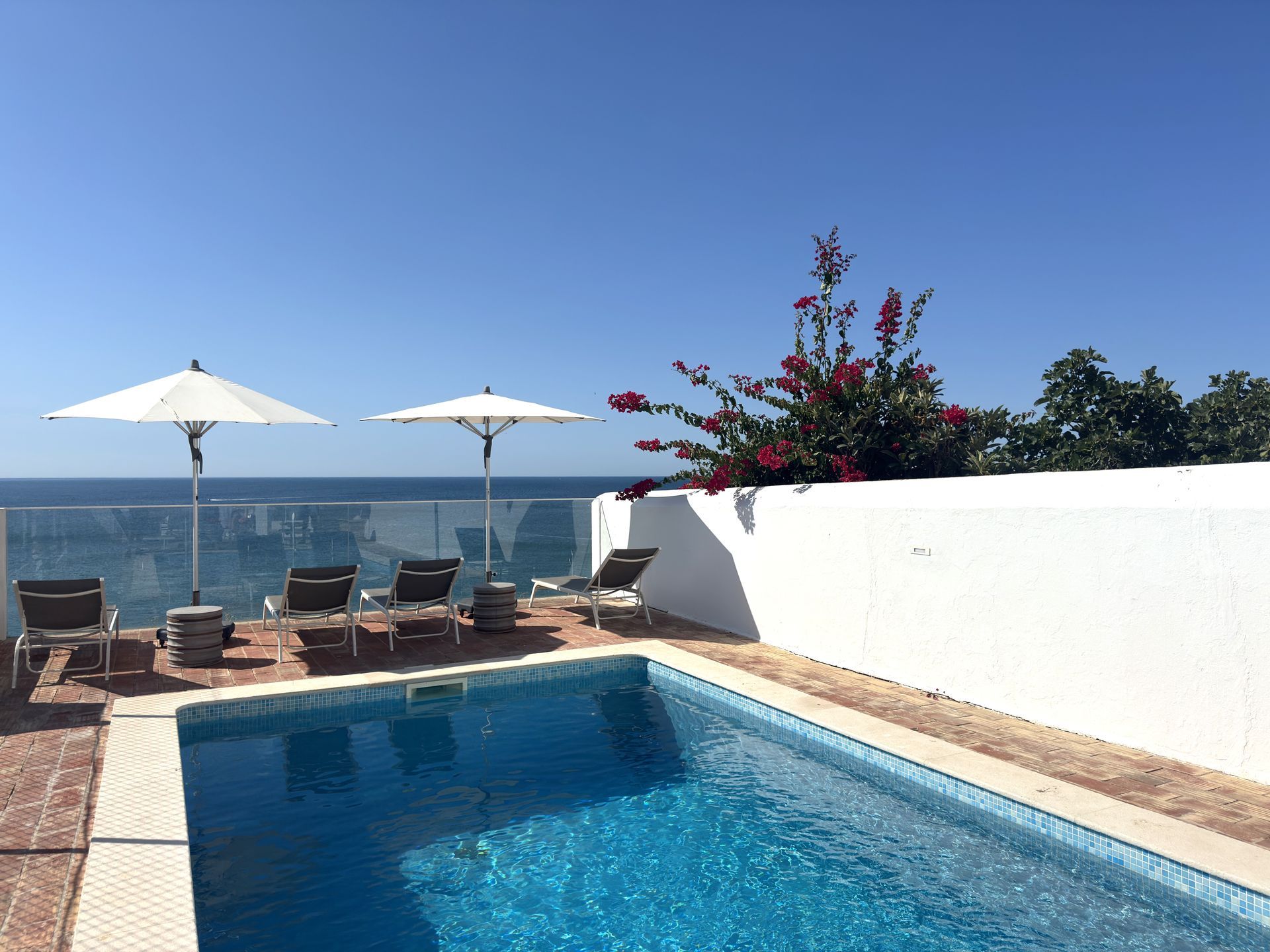 Uma piscina cercada por cadeiras e guarda-sóis com vista para o oceano