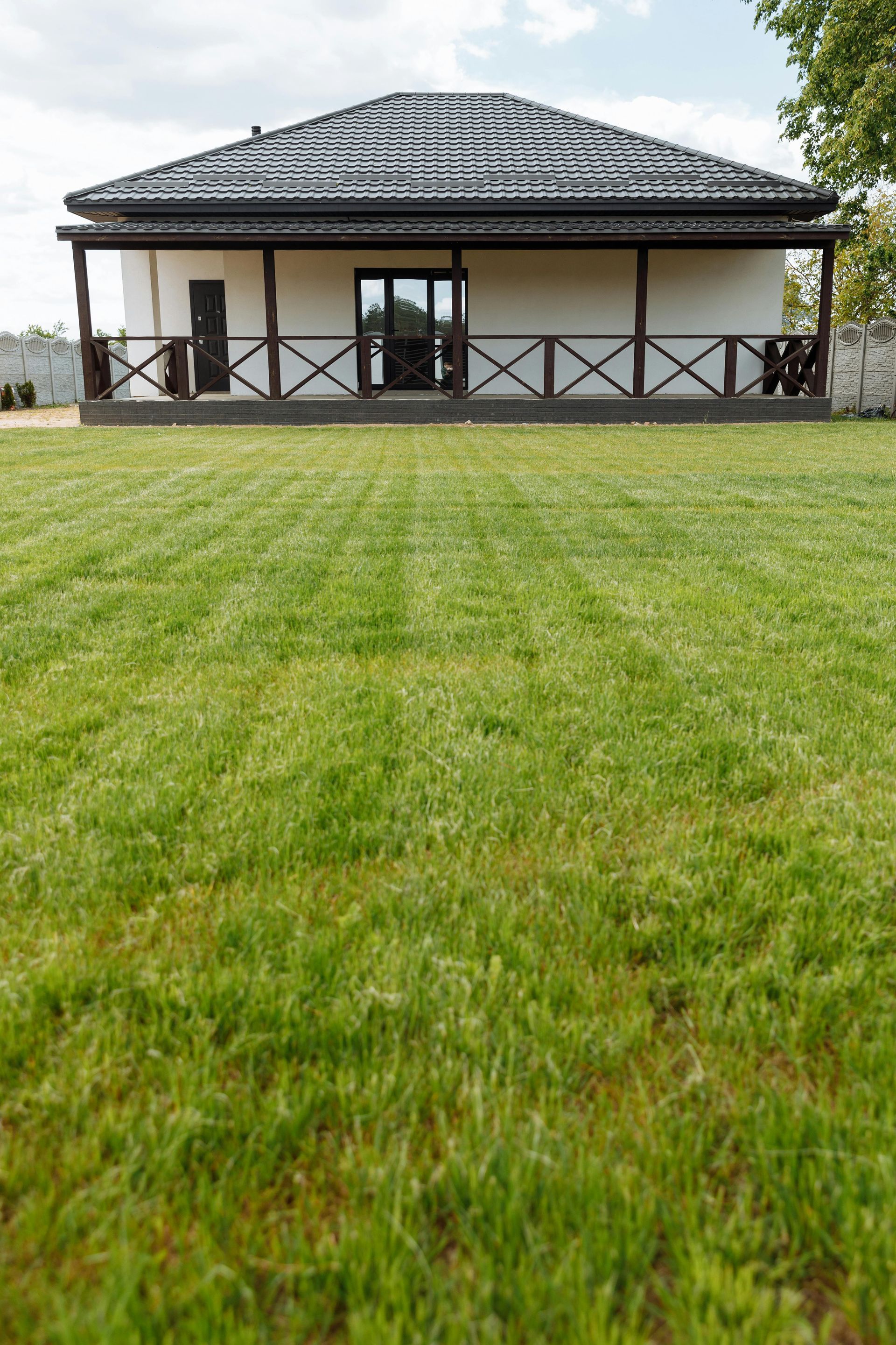 Single-story house with a dark roof and porch, viewed across a large green lawn