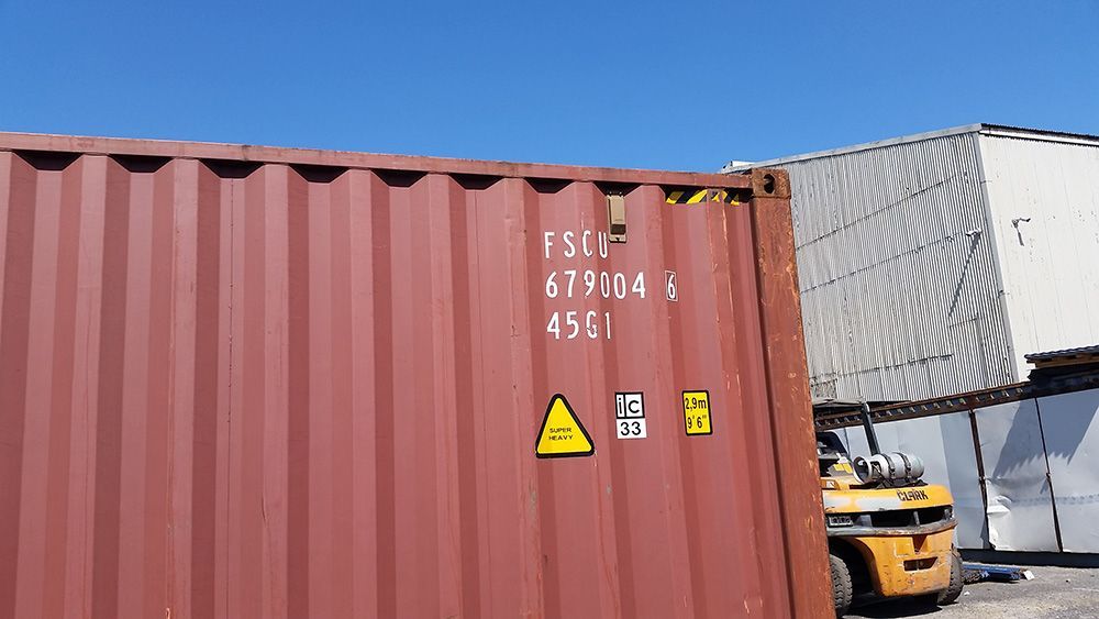 A Red Shipping Container With A Yellow Forklift Parked Next To It — Oz Shipping Containers in Teralba, NSW
