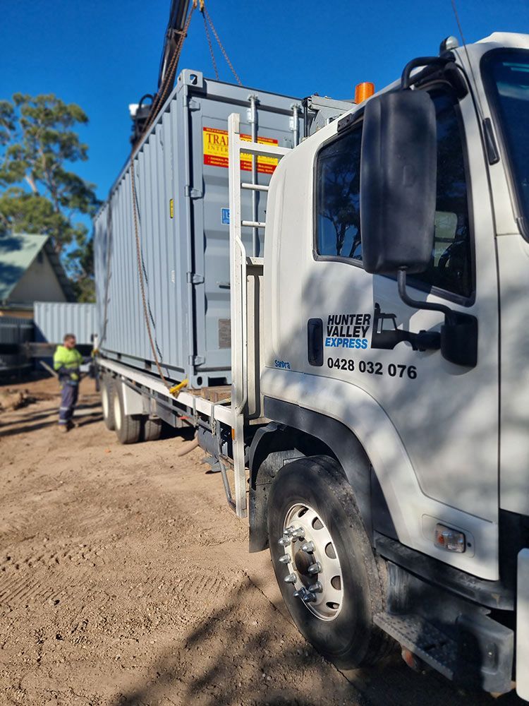 A White Truck Is Carrying A Container With A Crane Attached To It — Oz Shipping Containers in Teralba, NSW