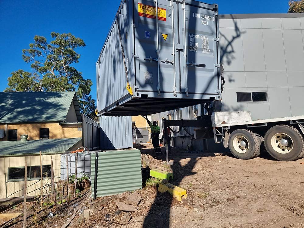 A Large Shipping Container Is Being Lifted By A Crane On Top Of A Truck — Oz Shipping Containers in Teralba, NSW