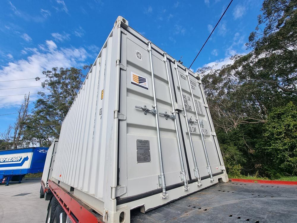 A White Shipping Container Is Sitting On Top Of A Tow Truck — Oz Shipping Containers in Teralba, NSW