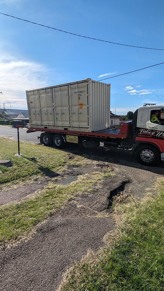 A Tow Truck Is Carrying A Shipping Container Down A Road — Oz Shipping Containers in Grafton, NSW