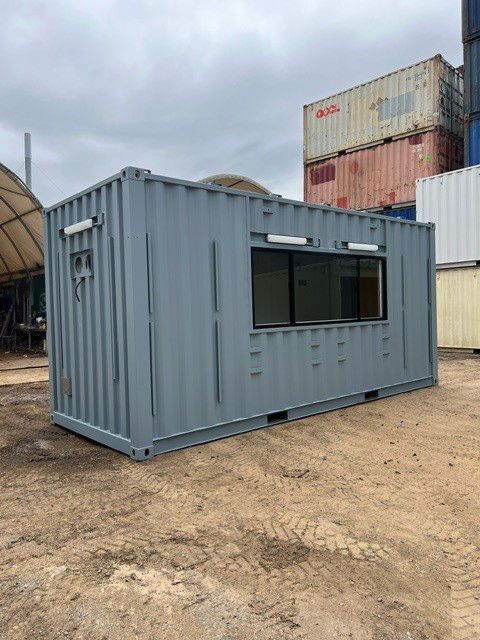 A Gray Shipping Container With A Window Is Sitting In A Dirt Field — Oz Shipping Containers in Teralba, NSW