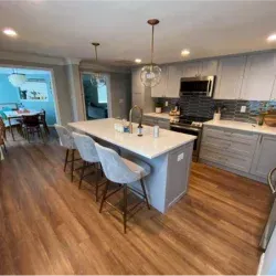 Modern kitchen with gray cabinets, island, stools, stainless steel appliances, and wood floors.