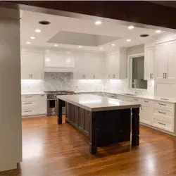 Modern kitchen with white cabinets, dark island, marble backsplash, and hardwood floors.