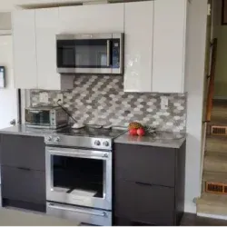 Modern kitchen with gray and white cabinets, stainless steel appliances, and honeycomb backsplash.