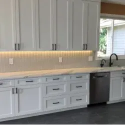 White kitchen cabinets with black hardware, a stainless steel dishwasher, and a marble countertop.
