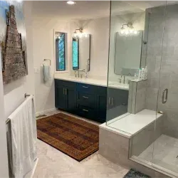 Modern bathroom with blue vanity, large shower, and rug.