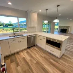 White kitchen with island, stainless steel appliances, and large window overlooking a field.