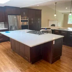 Modern kitchen with dark cabinetry, large island with cooktop, and stainless steel appliances.
