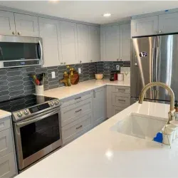 Modern kitchen with gray cabinets, stainless steel appliances, and white countertops.