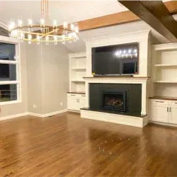 Living room with fireplace, built-in shelves, and hardwood floor. Gold chandelier hangs above.