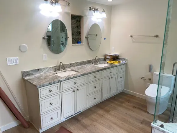 Bathroom with a white vanity, dual sinks, oval mirrors, and a glass shower door.
