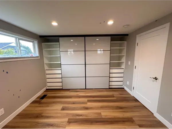 Bedroom with built-in closet, white doors, shelves, drawers, wood floor, gray walls, and a window.