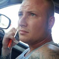 Man holding a pen near his face, sitting in a car; looking pensively.