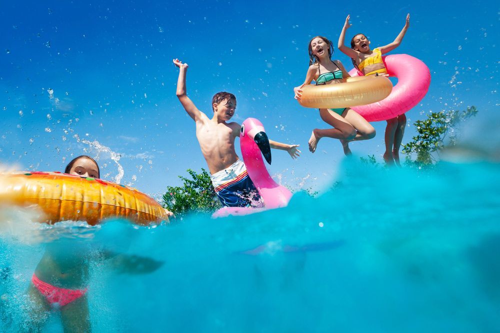 A Group of People Are Jumping Into a Swimming Pool With Floats — Taree Pool Supplies in Taree, NSW