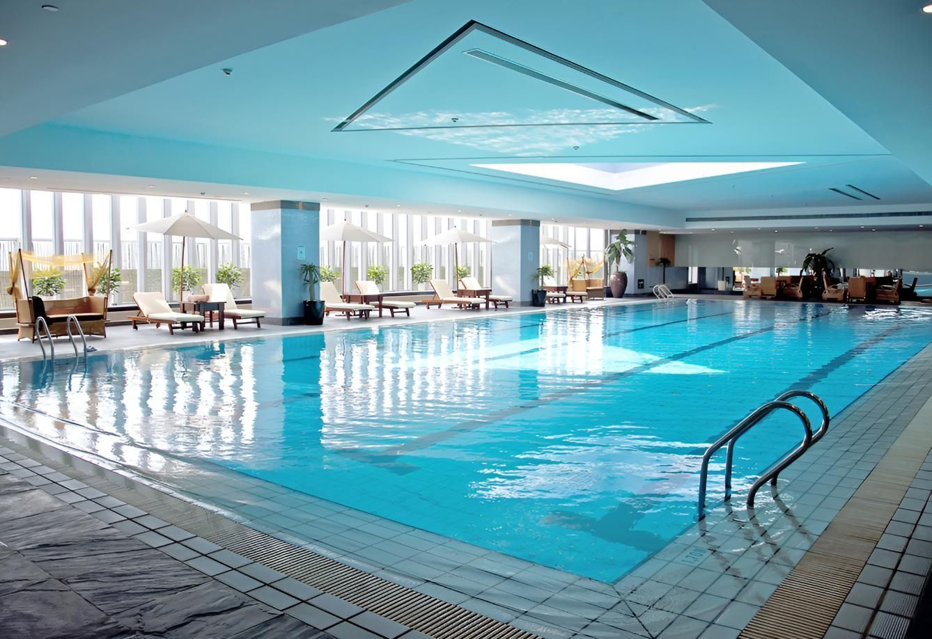 A Large Indoor Swimming Pool With Chairs and Umbrellas Around It — Taree Pool Supplies in Taree, NSW
