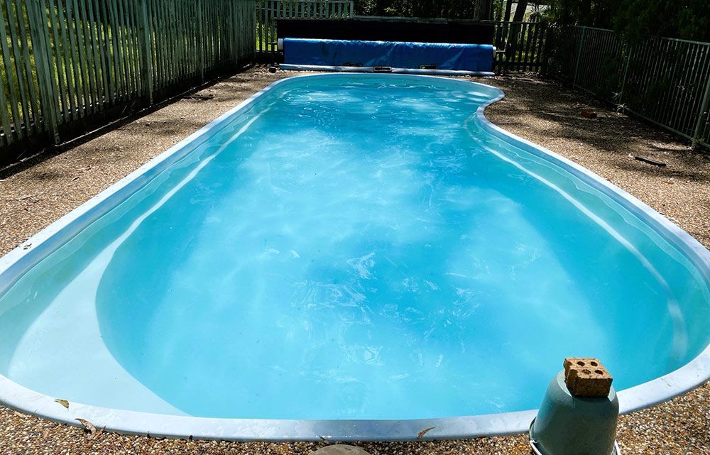 A Large Swimming Pool Filled With Blue Water in a Backyard — Taree Pool Supplies in Taree, NSW