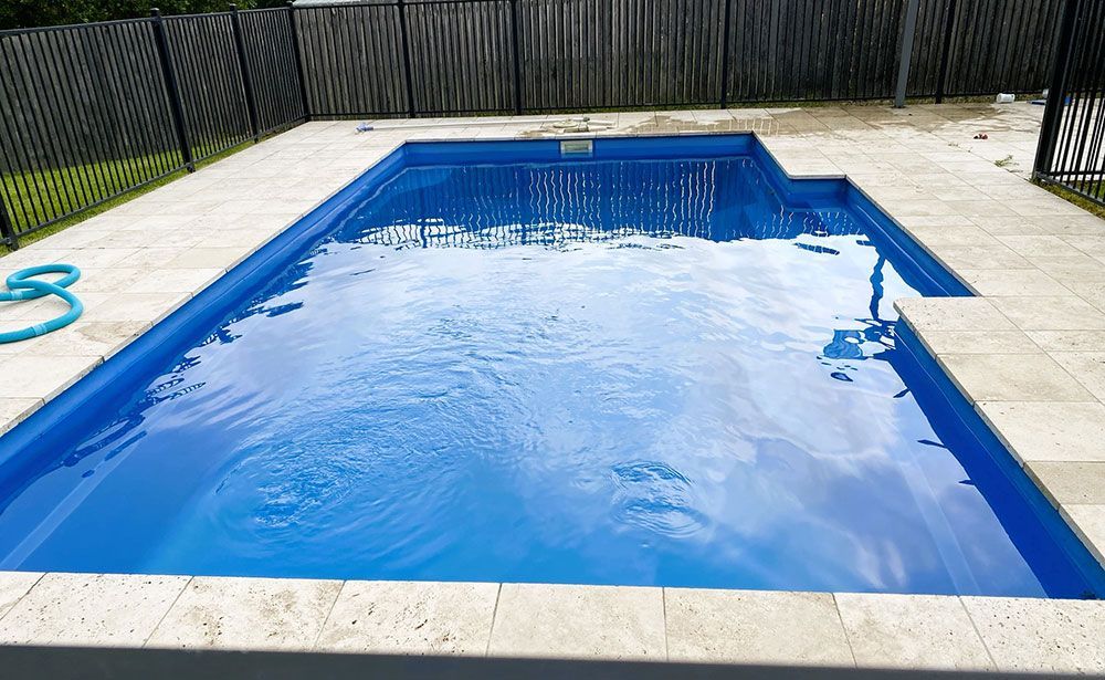 A Large Blue Swimming Pool is Surrounded by a Fence and a Hose — Taree Pool Supplies in Taree, NSW