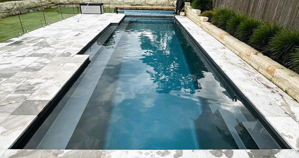 A Large Swimming Pool is Surrounded by a Patio and a Fence — Taree Pool Supplies in Harrington, NSW