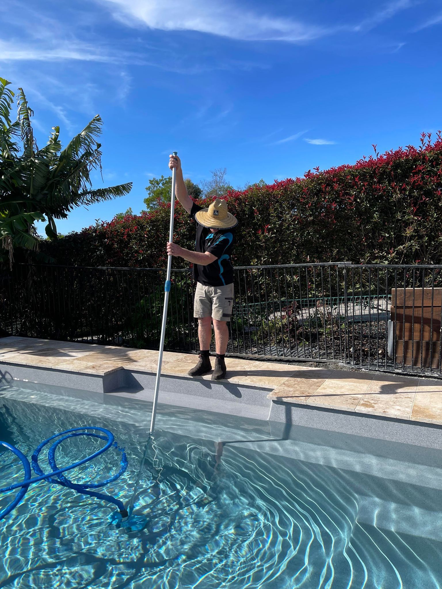 A Man is Cleaning a Swimming Pool With a Vacuum Cleaner — Taree Pool Supplies in Taree, NSW