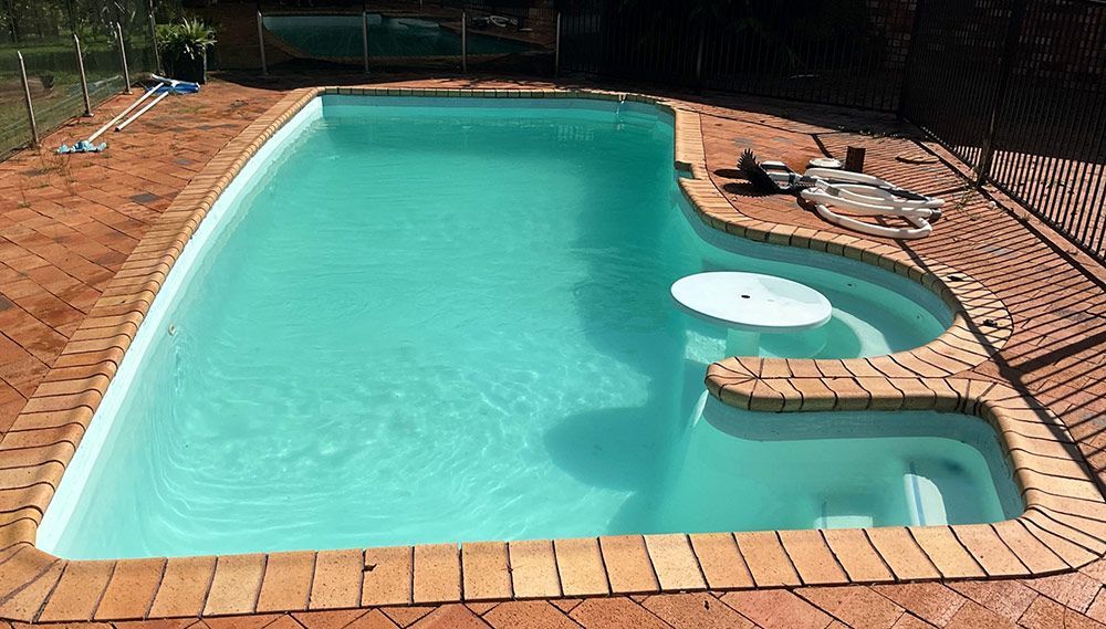 A Large Swimming Pool is Surrounded by Bricks and a Fence — Taree Pool Supplies in Wingham, NSW
