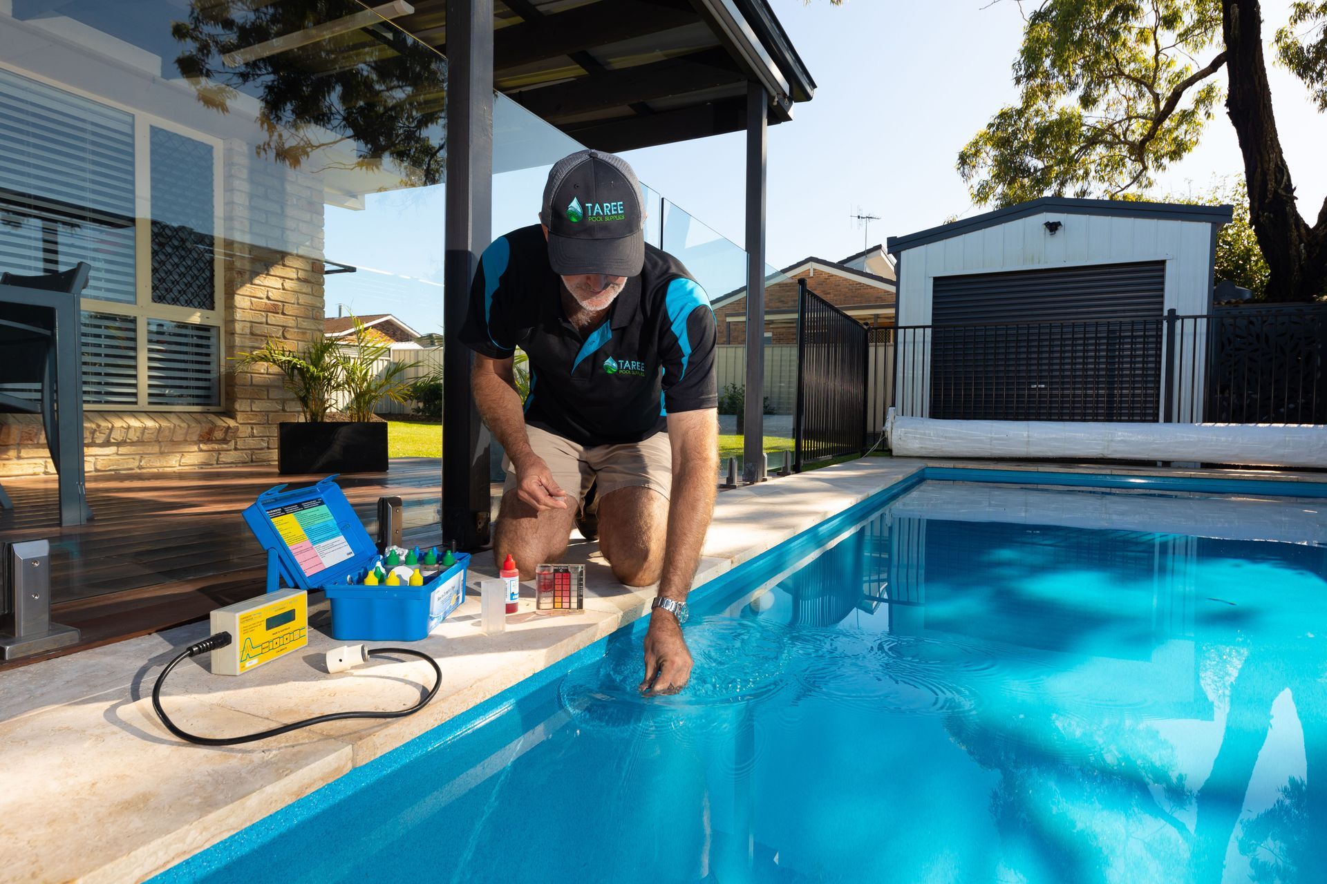 A Man is Kneeling on the Side of a Swimming Pool — Taree Pool Supplies in Taree, NSW