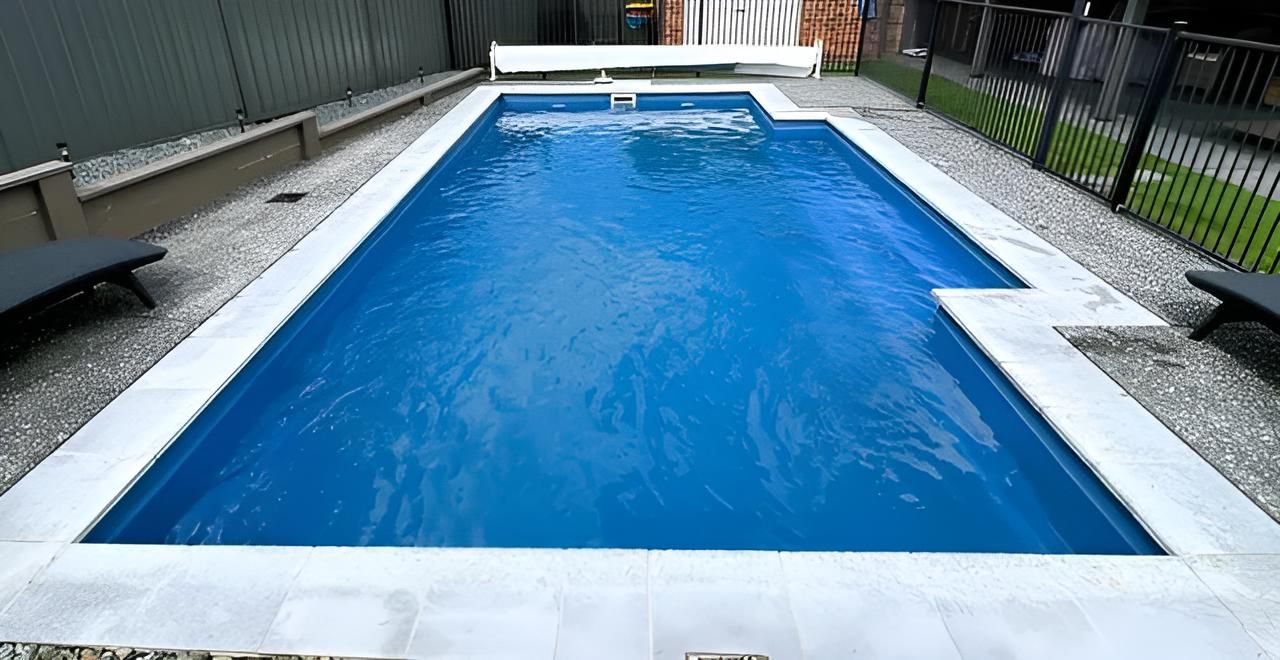 A Large Blue Swimming Pool is Surrounded by Gravel and a Fence — Taree Pool Supplies in Taree, NSW