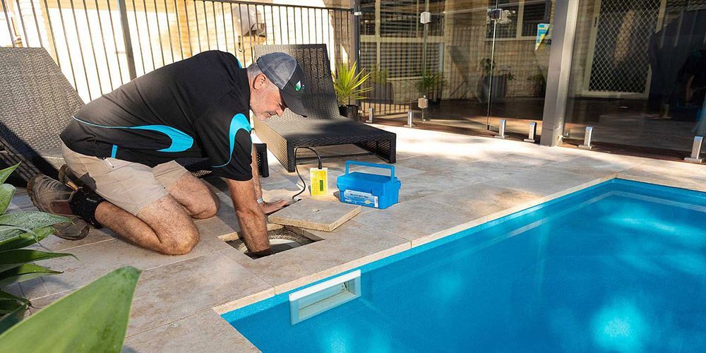 A Man is Kneeling Next to a Swimming Pool — Taree Pool Supplies in Taree, NSW