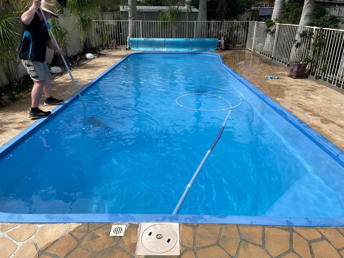 A Man is Cleaning a Swimming Pool With a Broom — Taree Pool Supplies in Old Bar, NSW