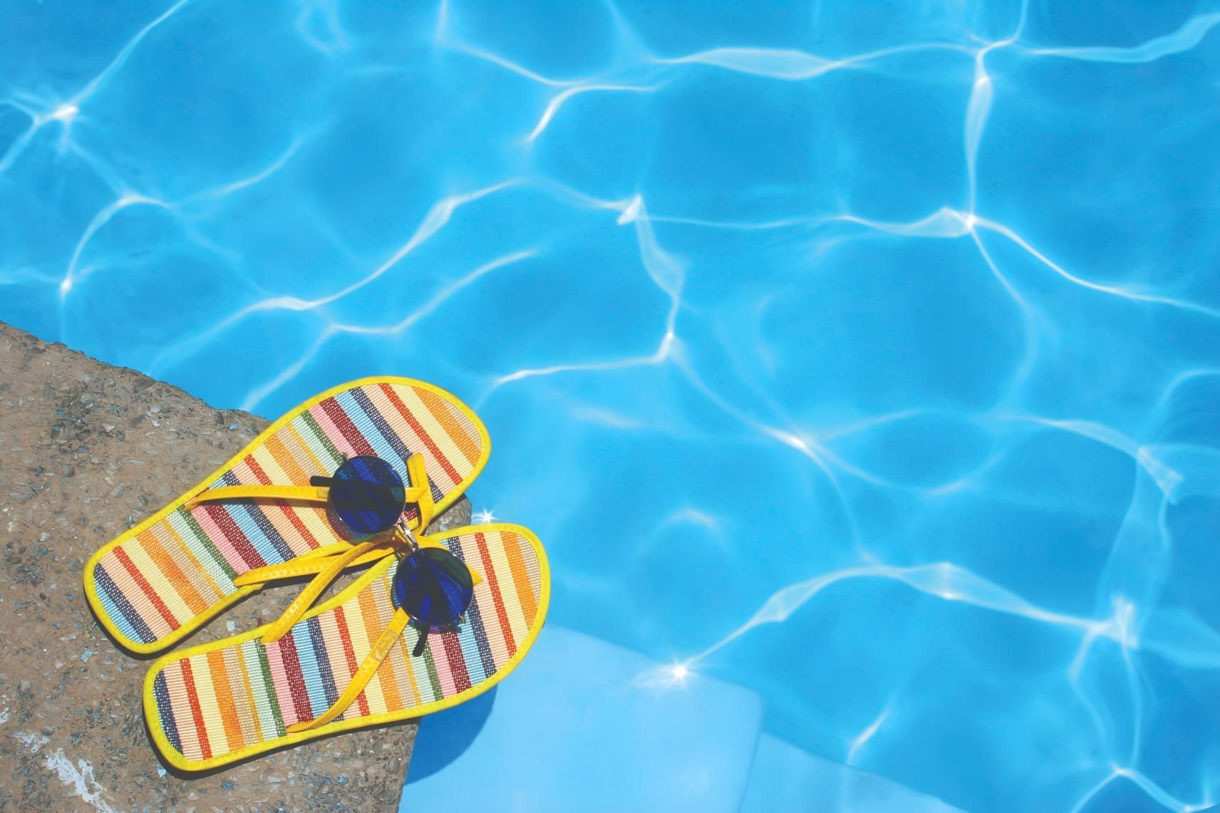 A Pair of Flip Flops and Sunglasses Are Sitting on the Edge of a Swimming Pool — Taree Pool Supplies in Taree, NSW