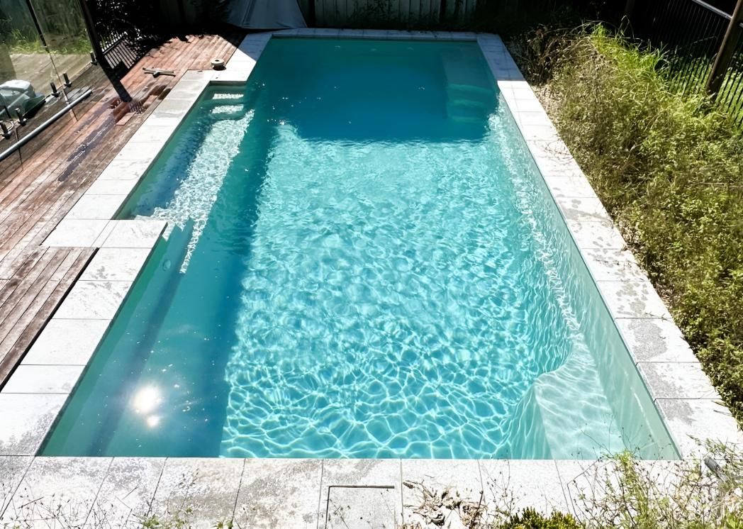 A Large Swimming Pool is Surrounded by Plants and a Wooden Deck — Taree Pool Supplies in Forster, NSW