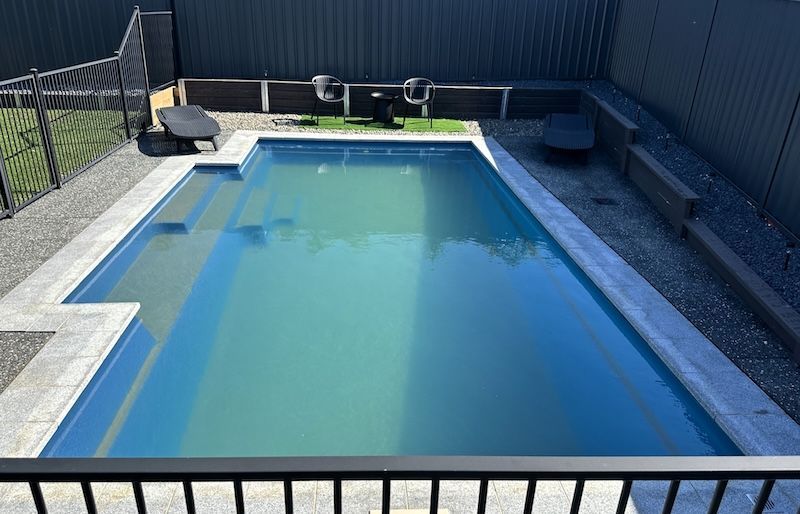 A Large Swimming Pool is Surrounded by a Fence and Chairs — Taree Pool Supplies in Taree, NSW