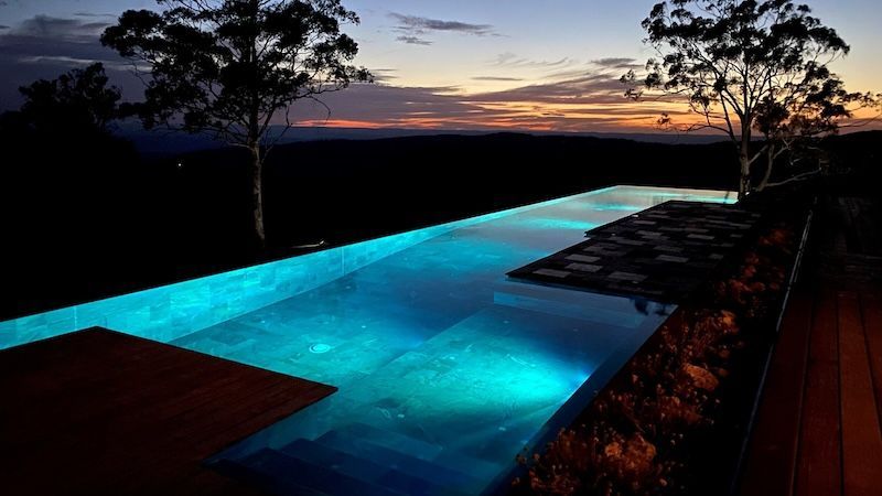 An Infinity Pool is Lit Up at Night With Trees in the Background — Taree Pool Supplies in Taree, NSW