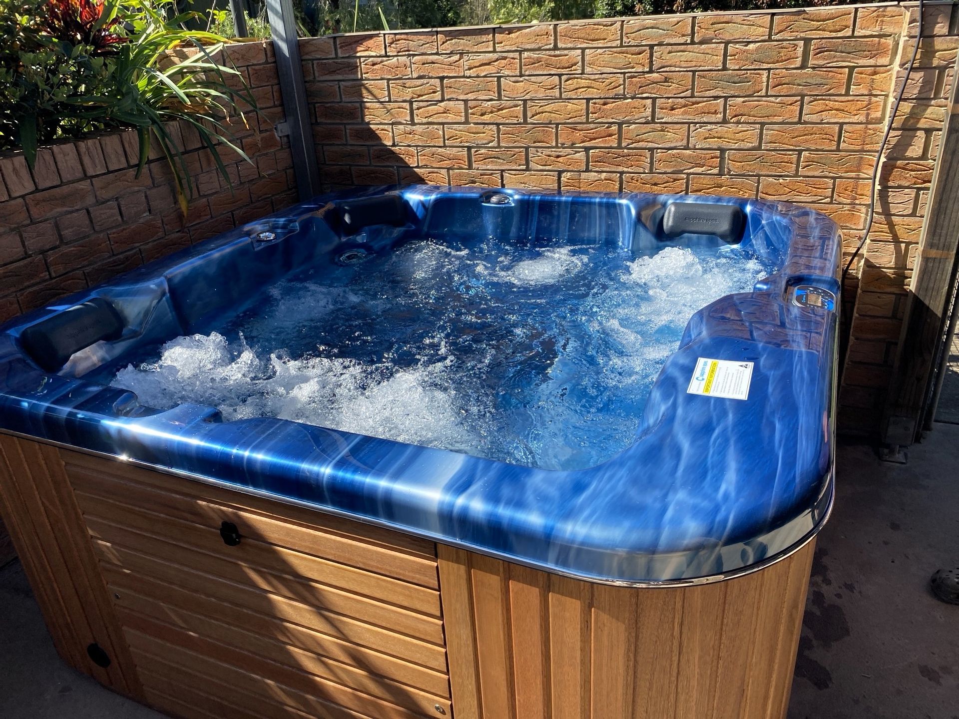 A Blue Hot Tub is Sitting in Front of a Brick Wall — Taree Pool Supplies in Taree, NSW