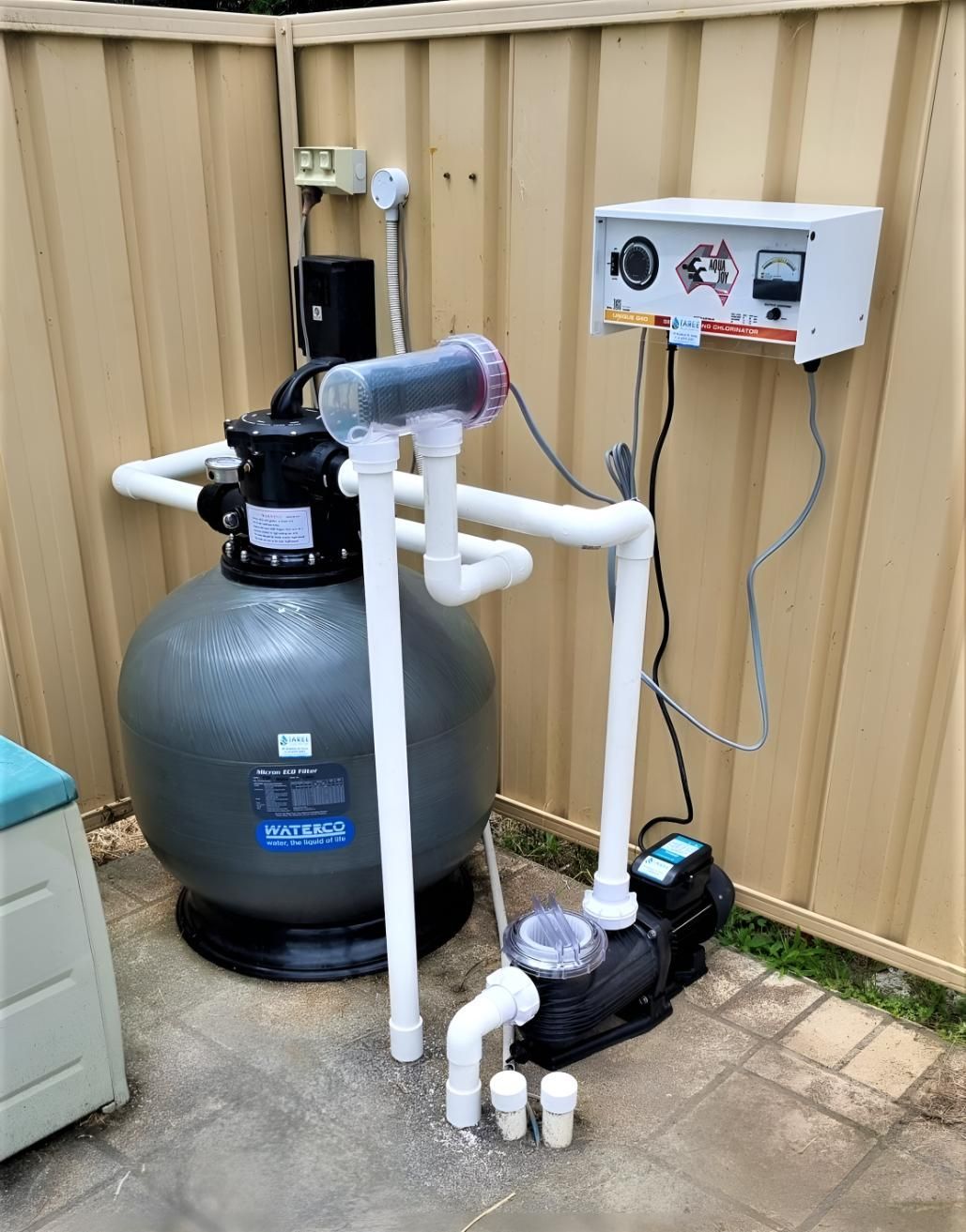 A Swimming Pool Filter is Sitting on the Ground Next to a Fence — Taree Pool Supplies in Forster, NSW
