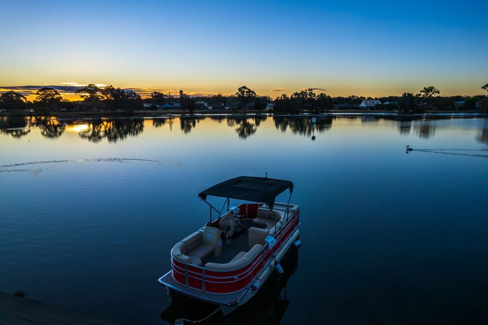 A Pontoon Boat is Floating on a Lake at Sunset — Taree Pool Supplies in Forster, NSW