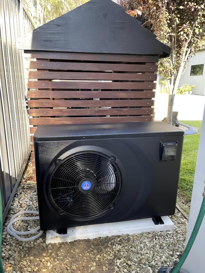 A Black Air Conditioner is Sitting in Front of a Wooden Shed — Taree Pool Supplies in Forster, NSW