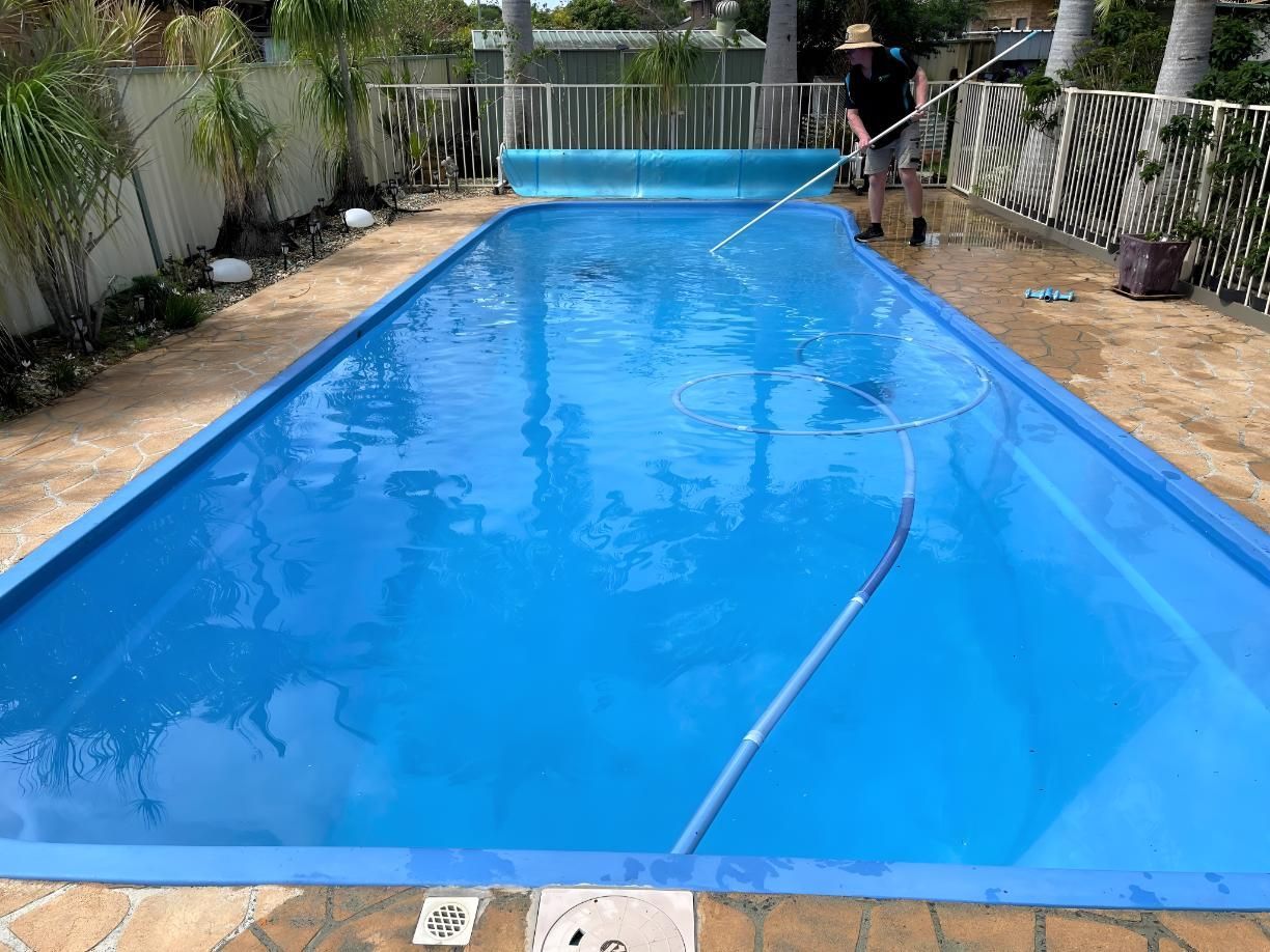 A Man is Cleaning a Large Swimming Pool With a Broom — Taree Pool Supplies in Forster, NSW