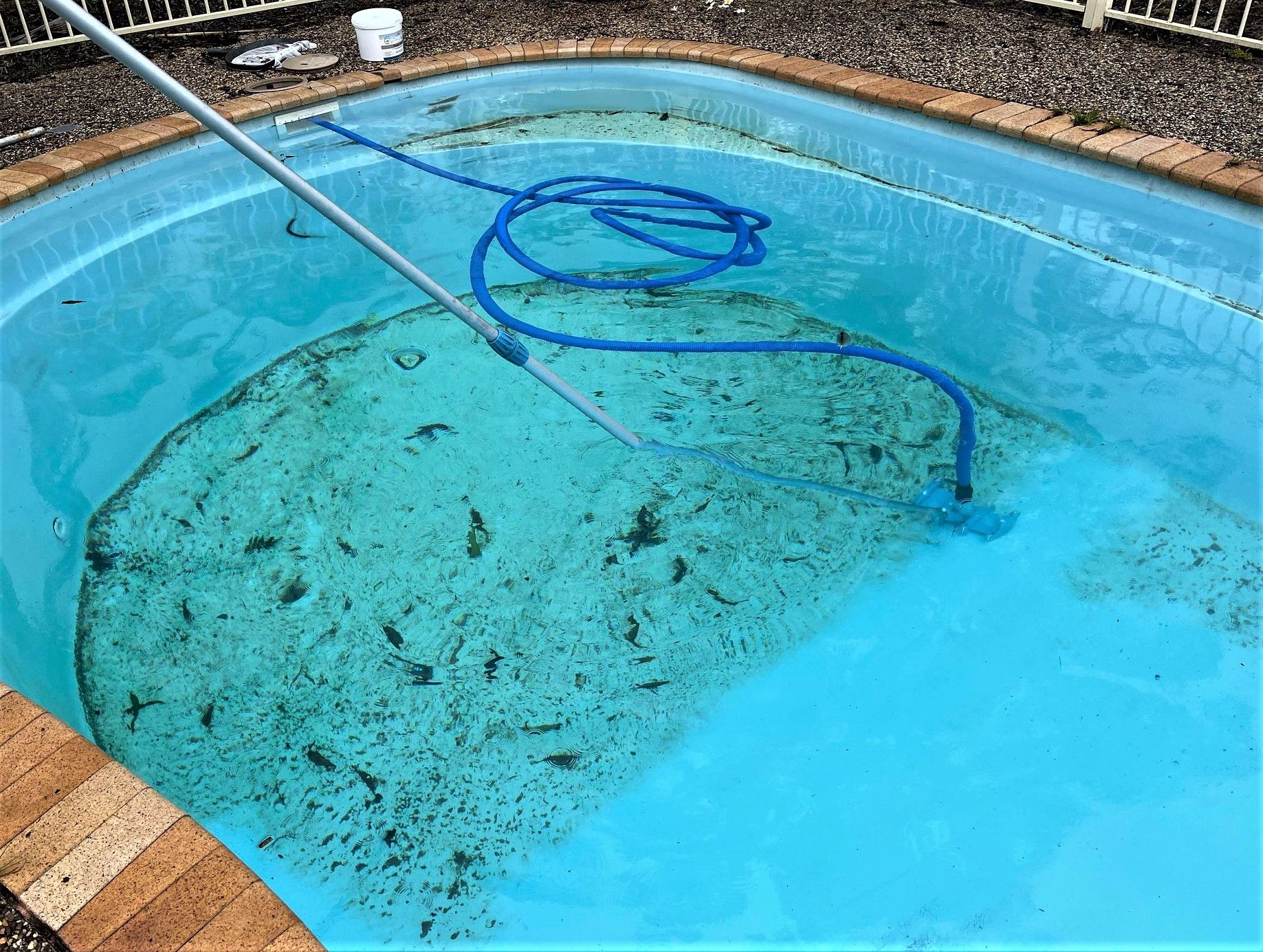 A Person is Cleaning a Swimming Pool With a Broom — Taree Pool Supplies in Taree, NSW